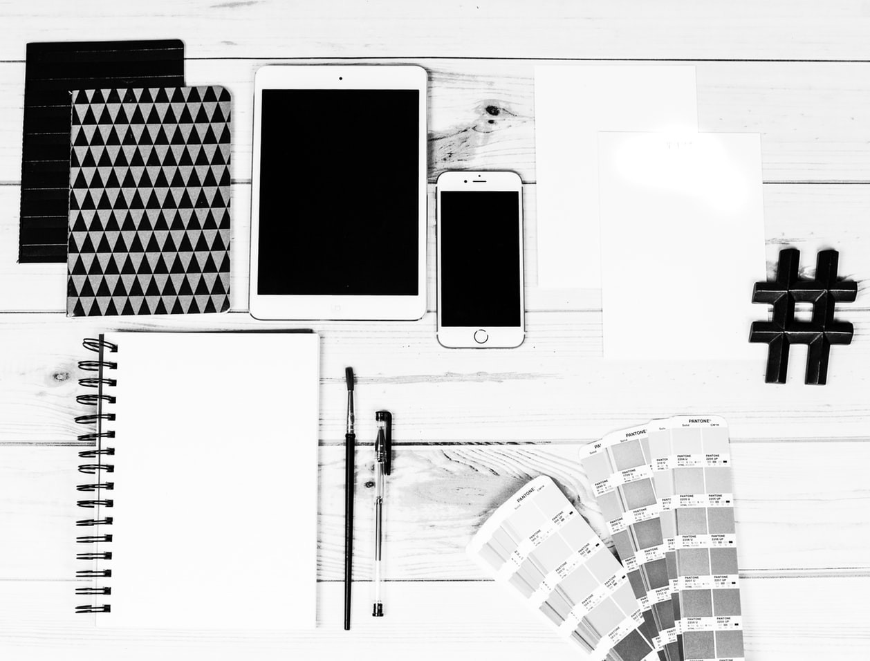Black and white image of mobile and computers on a wood table